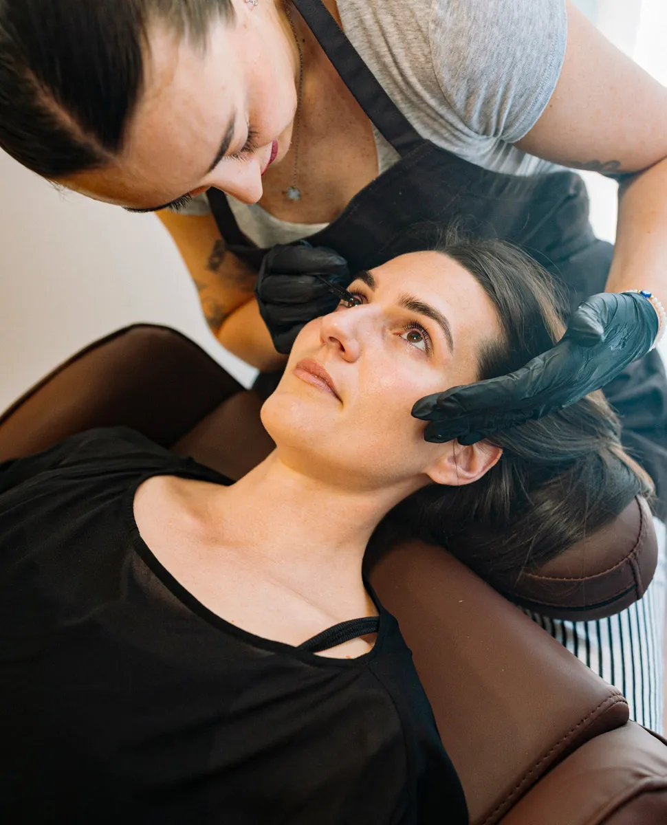Brow technician shaping a client's brows with tweezers at Olaya & Co. in Byron Bay