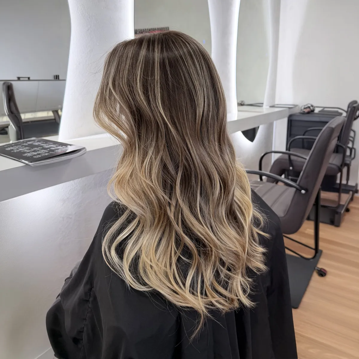 Long brunette-to-blonde balayage with a soft, dark root melting into creamy blonde waves — after