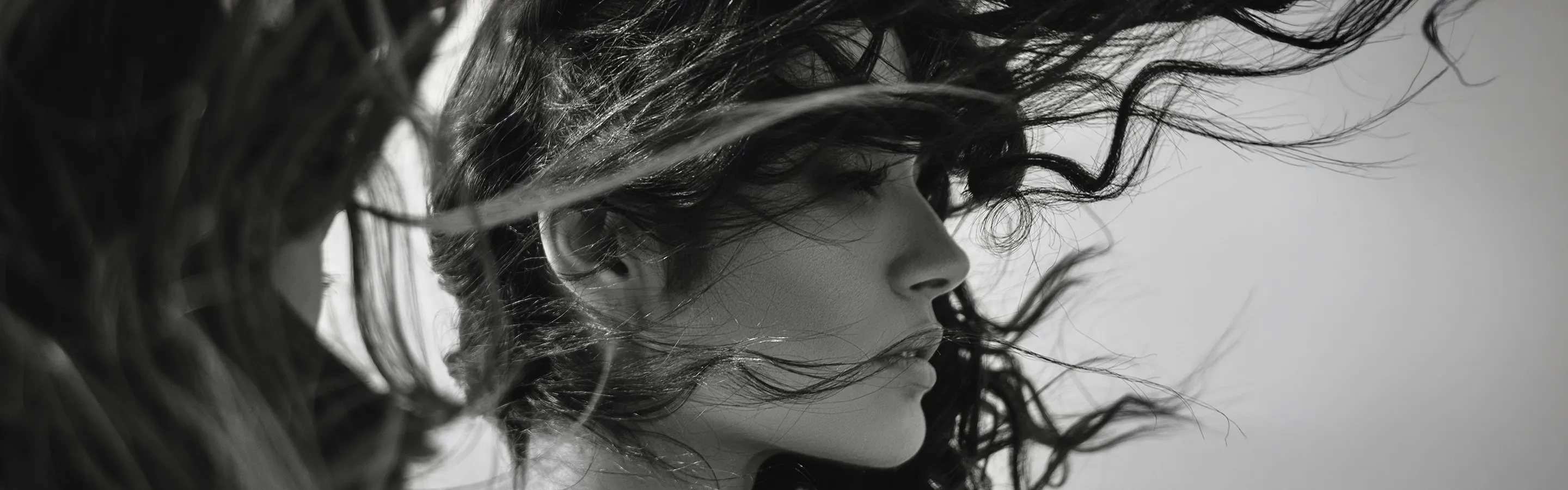 Black-and-white profile of a woman with long, dark lashes, her curly hair swept across her face by the wind