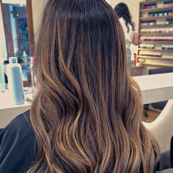 Back view of long dark hair with caramel balayage and soft waves