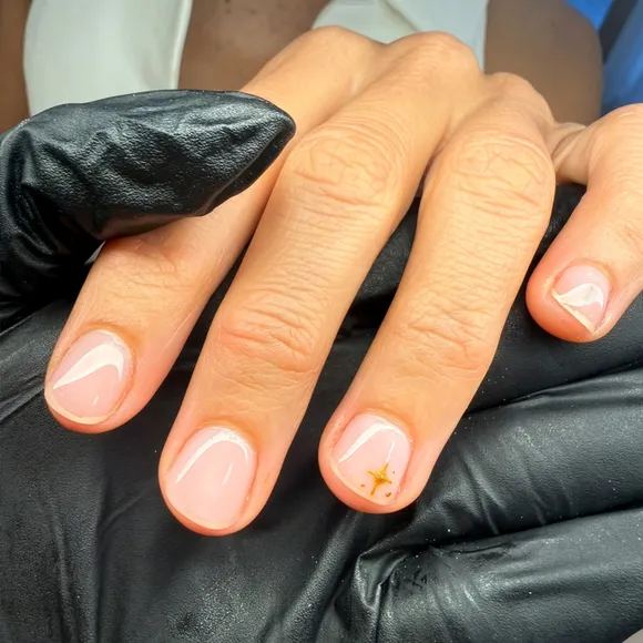 Close up of short sheer pink nails with a tiny gold star accent