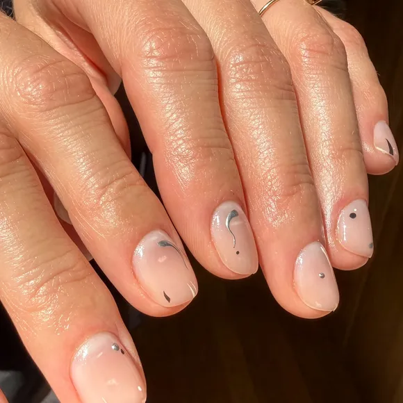 Close up of short nude nails with minimalist silver swirls and dots