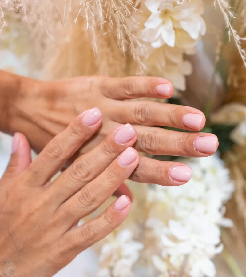 Glossy brick-red manicure on short square nails, hands holding a green leaf