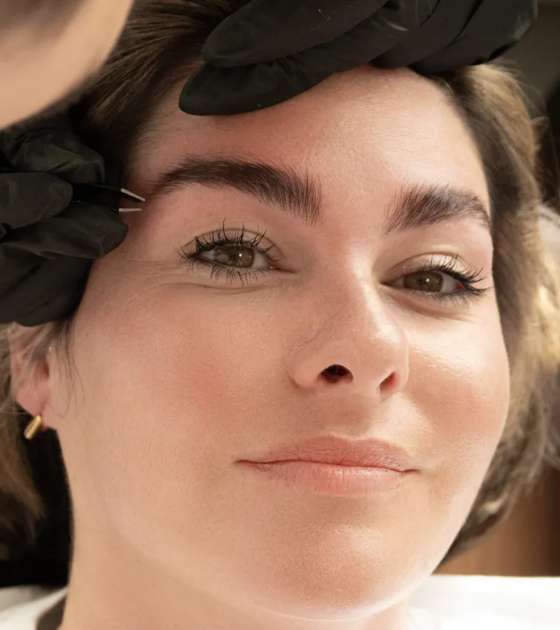 Technician applying brow lamination lotion while the client relaxes with eyes closed