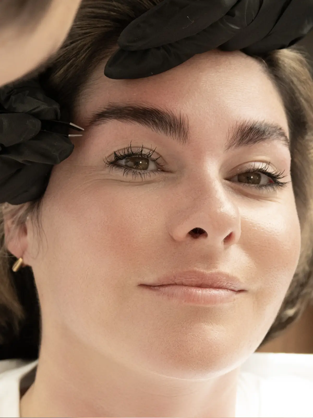 Gloved hand tweezing to shape a client's full, natural brows