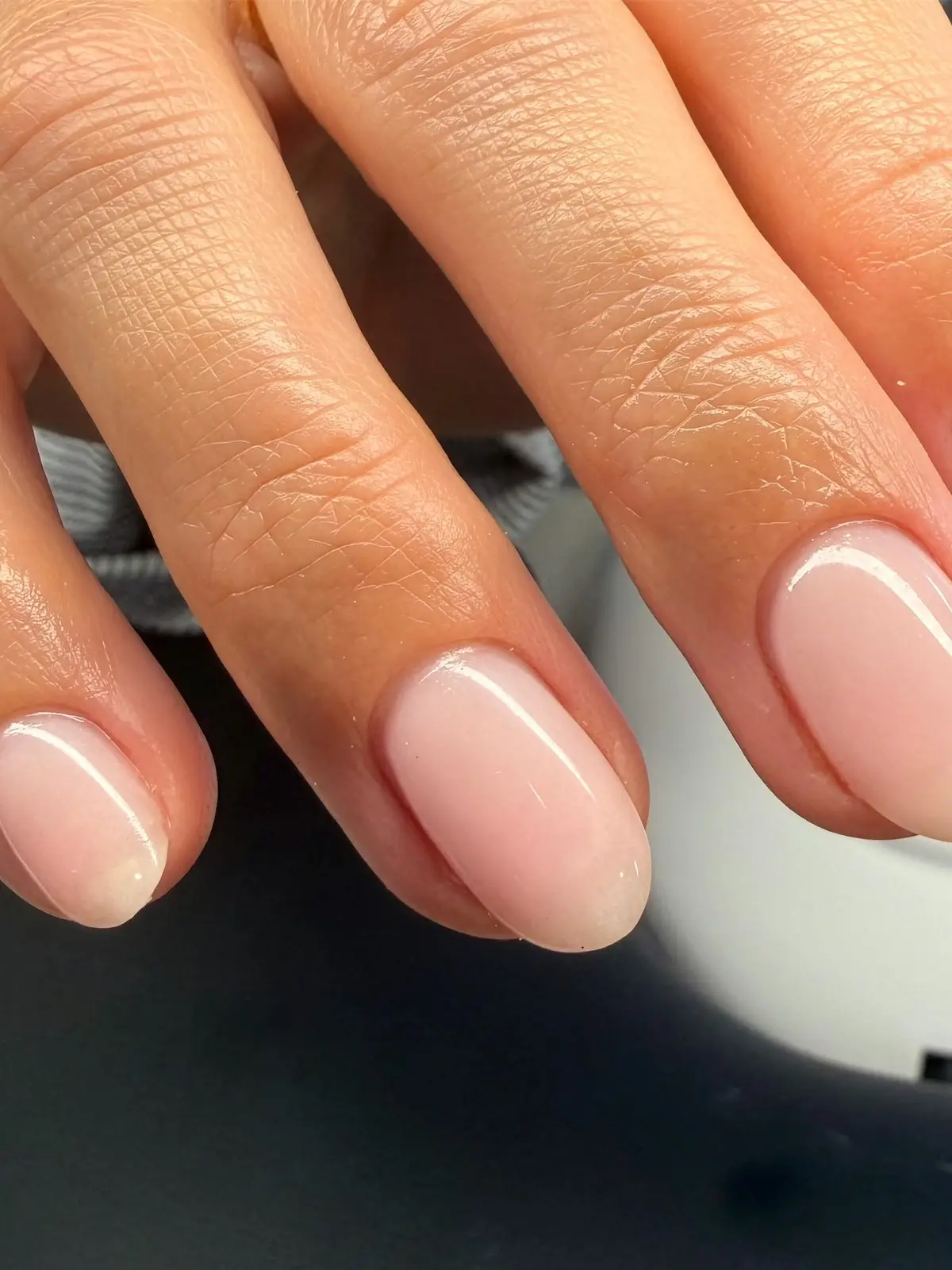 Close-up of short rounded nails with a glossy natural pink finish