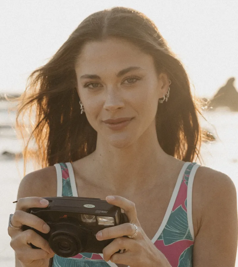 Natural bronzed makeup with defined brows, model posing against a coastal backdrop